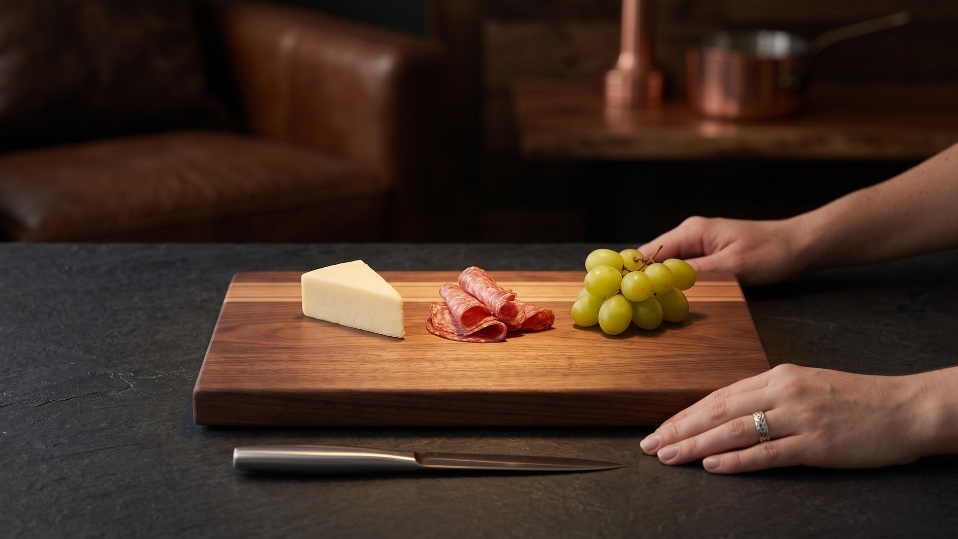 Charis Studios edge-grain cutting board featuring walnut, cherry, and maple stripes with cheese, salami, and grapes.
